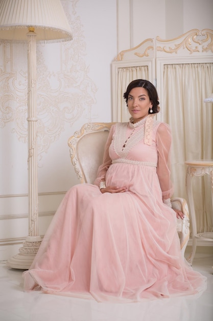 Photo gratuite heureuse femme enceinte brune qui a l'air excitée parce qu'elle attend un bébé dans un intérieur vintage dans un appartement cher ou riche.