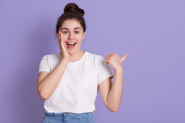 Heureuse femme heureuse souriante touchant sa joue avec la paume et pointant de côté avec le pouce