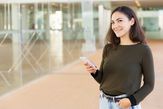 Heureuse femme latine amicale tenant un téléphone portable et souriant