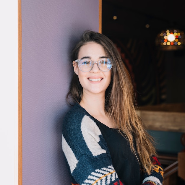 Heureuse femme à lunettes debout au mur