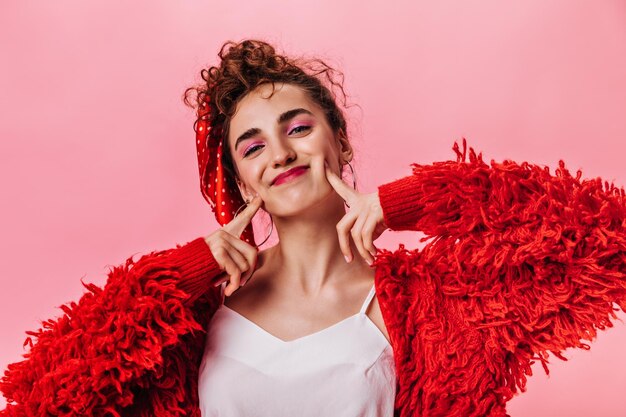 Heureuse femme en manteau moelleux et haut blanc souriant sur fond rose