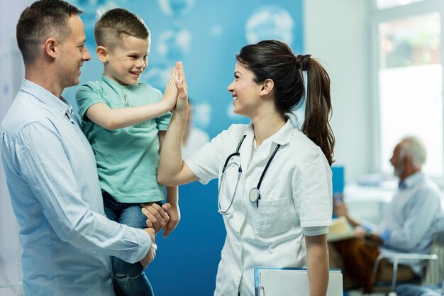Heureuse femme médecin donnant une haute fie à un petit garçon qui est venu avec son père à l'hôpital