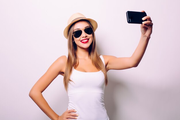 Heureuse femme mignonne faisant selfie isolé sur mur gris.