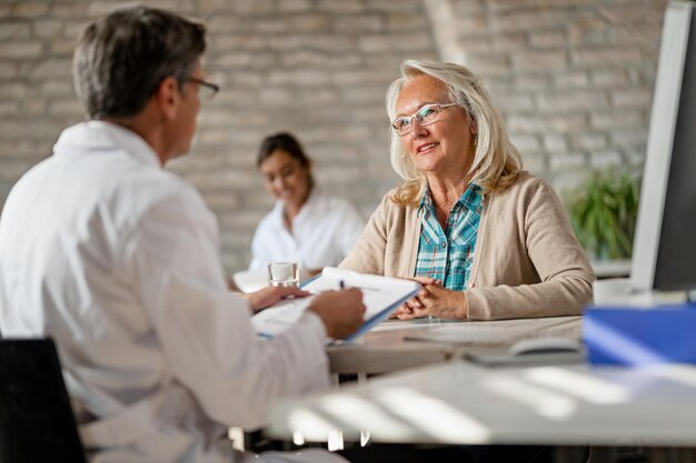 Heureuse femme mûre ayant des consultations avec son médecin et parlant des possibilités d'assurance médicale à la clinique
