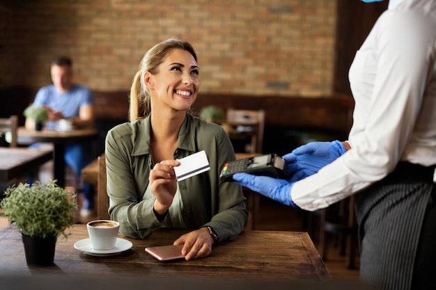 Heureuse femme payant par carte de crédit dans un café pendant l'épidémie de virus