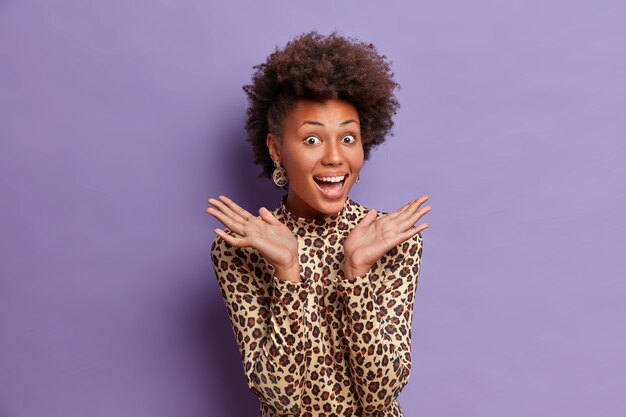 Heureuse femme à la peau foncée avec des cheveux naturels bouclés, lève les paumes de joie, sourit largement, entend d'excellentes nouvelles