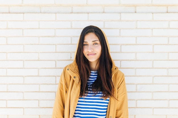 Heureuse femme portant veste debout contre le mur de briques