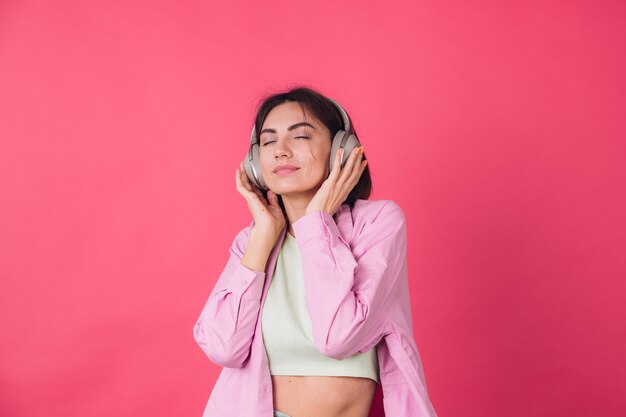 Heureuse femme positive dans les écouteurs sur le mur rouge rose