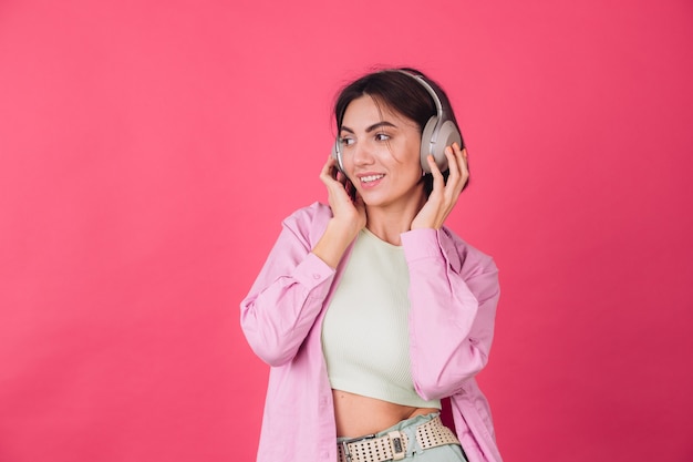 Heureuse femme positive dans les écouteurs sur le mur rouge rose