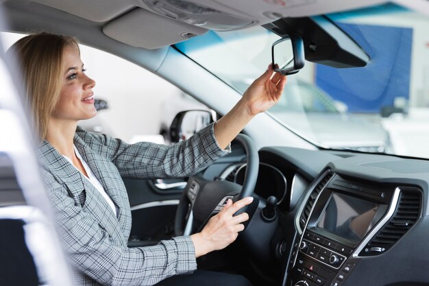 Heureuse femme regarde dans le rétroviseur de la voiture