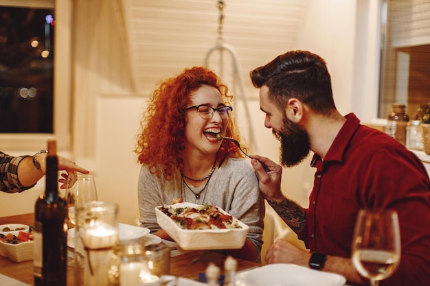 Heureuse femme rousse s'amusant tout en étant nourrie par son petit ami à table à manger