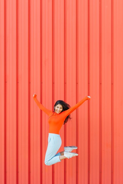 Heureuse femme sautant sur un fond ondulé rouge tandis que le bras tendu