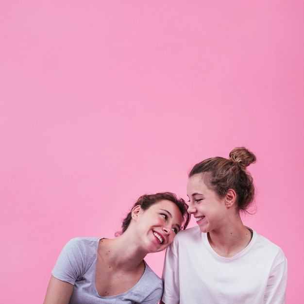 Heureuse femme se penchant sur l&#39;épaule de la femme sur fond rose