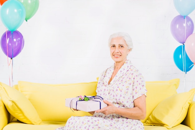 Heureuse femme senior assise sur un canapé avec un cadeau d&#39;anniversaire