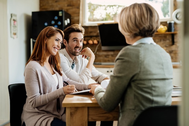 Heureuse femme signant un document tout en étant avec son mari lors d'une réunion avec un agent d'assurance