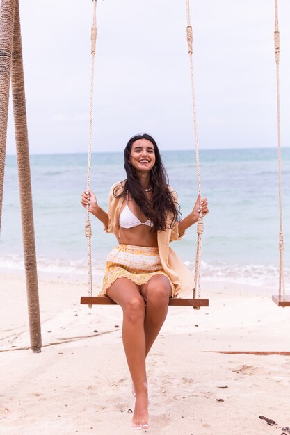 Heureuse femme souriante sur la balançoire à la plage, lumière chaude du jour.