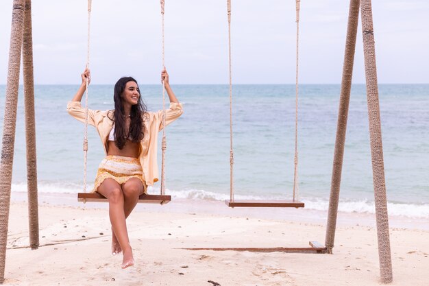 Heureuse femme souriante sur la balançoire à la plage, lumière chaude du jour.