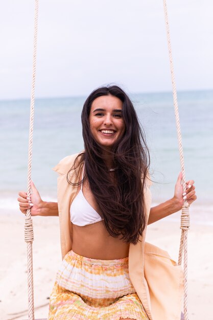 Heureuse femme souriante sur la balançoire à la plage, lumière chaude du jour.