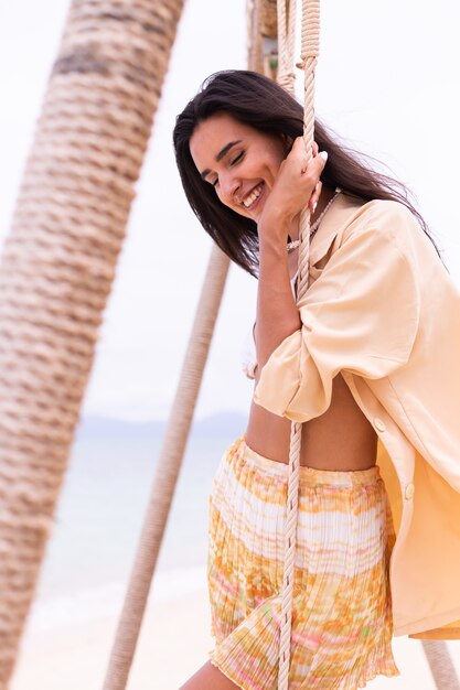 Heureuse femme souriante sur la balançoire à la plage, lumière chaude du jour.