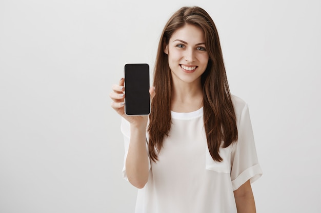 Heureuse femme souriante montrant l'écran mobile, recommande l'application ou le site commercial
