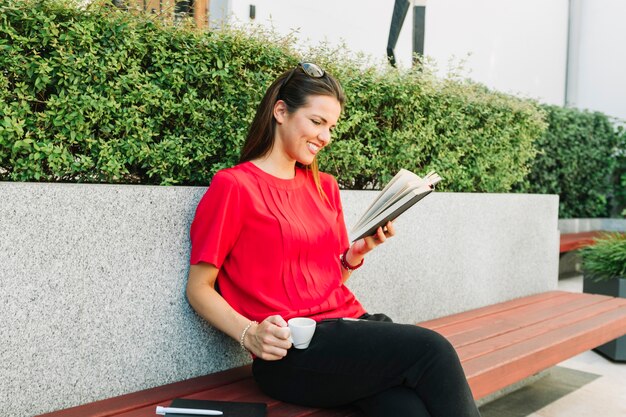 Heureuse femme avec une tasse de café, livre de lecture