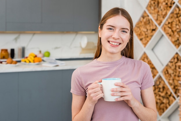 Heureuse femme tenant une tasse dans la cuisine