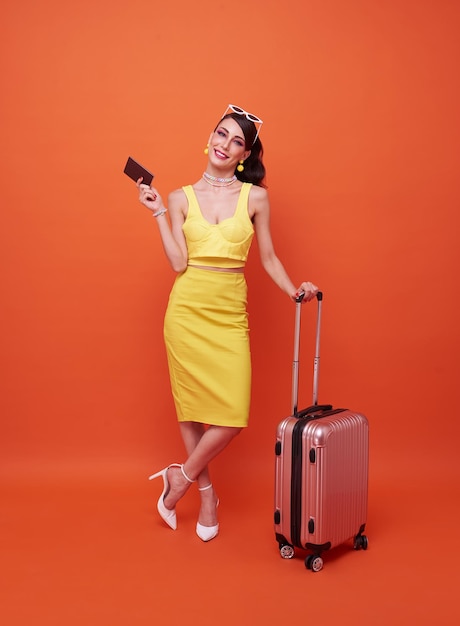 Heureuse femme tenant une valise et montrant un passeport sur fond orange