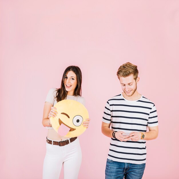 Heureuse femme tenant des yeux emoji clin d&#39;oeil près de son ami avec téléphone portable