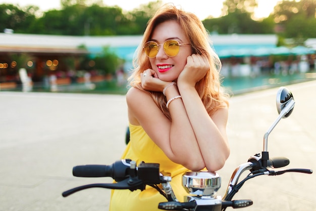 Heureuse Femme Tête Rouge En Robe Jaune Se Détendre Sur Son Scooter électrique Tout En Passant Des Vacances Dans La Ville Moderne. Humeur Romantique.