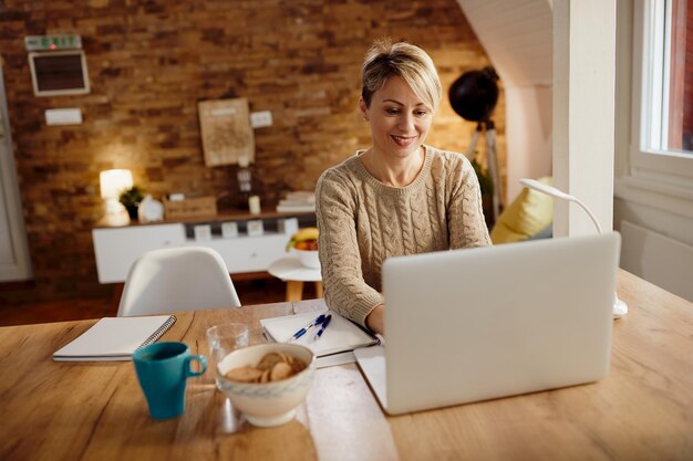 Heureuse femme utilisant un ordinateur portable tout en travaillant à la maison