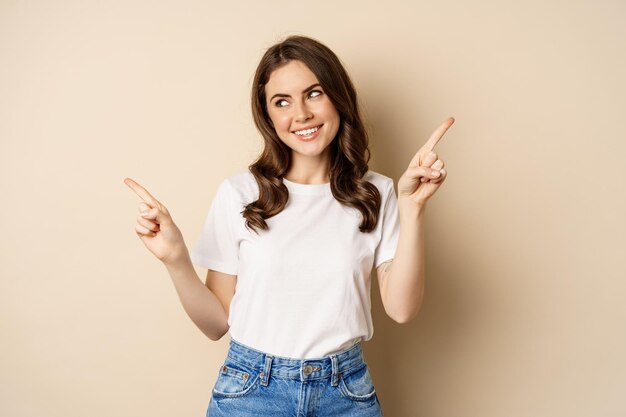 Heureuse fille authentique souriante pointant les doigts sur le côté montrant la bannière gauche et droite démontrant p...