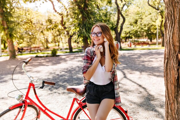 Heureuse fille aux cheveux bruns profitant du week-end en été Photo extérieure d'une femme blanche joyeuse posant dans un parc à vélo