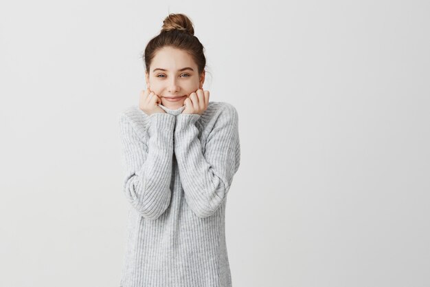 Heureuse fille caucasienne à la mode étant satisfaite et heureuse. Étudiante se reposant à la maison après les cours s'enveloppant dans un col de chandail gris. Concept de bonheur et de plaisir