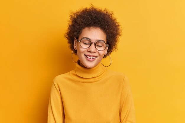 heureuse fille millénaire sincère avec des cheveux bouclés beauté naturelle sourit doucement avec les yeux fermés obtient compliment aime la vie porte poloneck occasionnel.