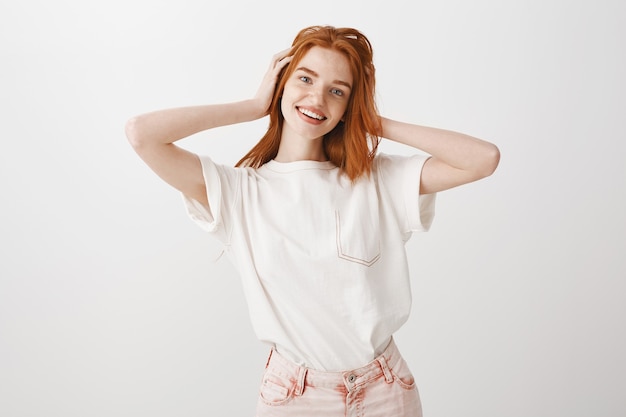 Heureuse fille rousse souriante et élégante touchant ses cheveux