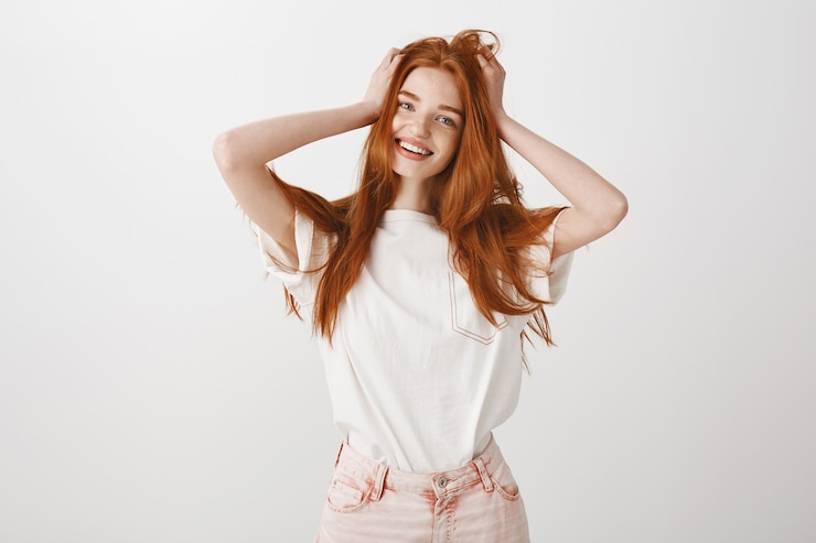 Photo gratuit heureuse fille rousse souriante touchant ses cheveux