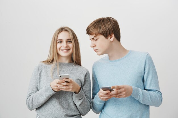 Heureuse fille souriante à l'aide de téléphone portable, mec regardant sérieusement son écran de smartphone