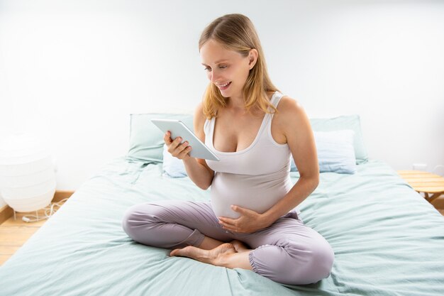 Heureuse future maman lisant sur l'écran de la tablette