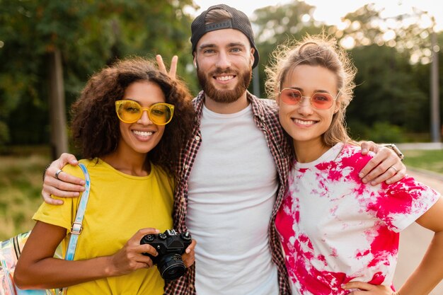 Heureuse jeune entreprise d'amis souriants émotionnels marchant dans le parc avec appareil photo, homme et femme s'amusant ensemble