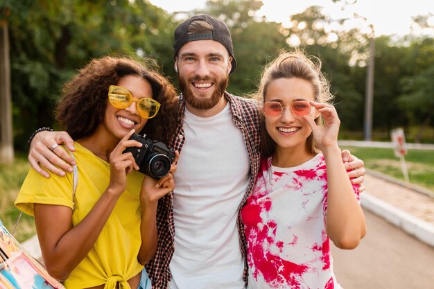 Heureuse jeune entreprise d'amis souriants émotionnels marchant dans le parc avec appareil photo, homme et femme s'amusant ensemble