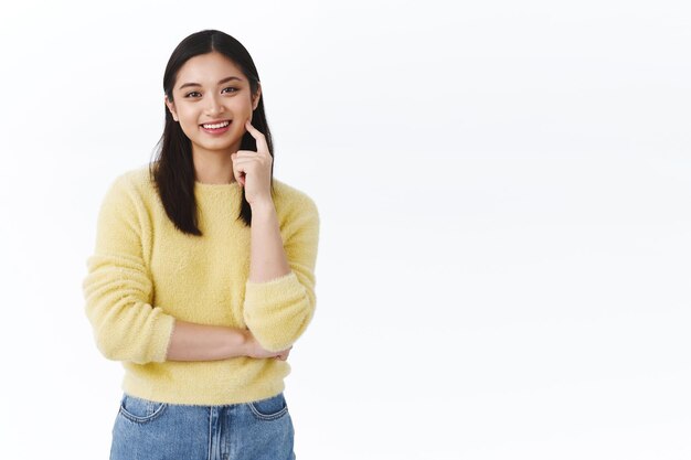 Heureuse jeune étudiante asiatique satisfaite touchant une peau propre et éclatante, souriante optimiste