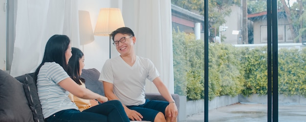 Heureuse jeune famille asiatique joue ensemble sur le canapé à la maison. Chinois mère père et fille enfant bénéficiant heureux se détendre passer du temps ensemble dans le salon moderne en soirée.