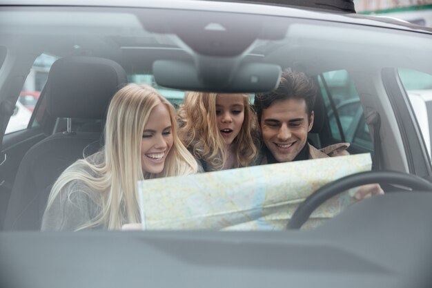 Heureuse jeune famille en voiture tenant la carte.