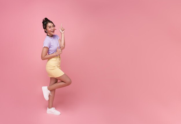 Heureuse jeune femme adolescente asiatique debout avec son doigt pointé isolé sur fond rose