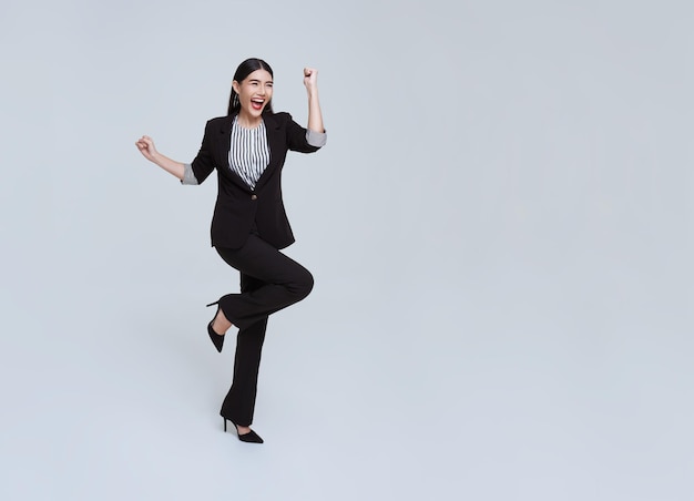 Heureuse jeune femme d'affaires asiatique joyeuse en costume sautant en l'air sur fond blanc de studio