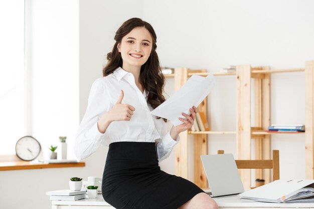 Heureuse jeune femme d'affaires ou secrétaire tenant un document dans un bureau moderne