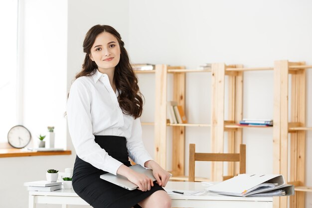 Heureuse jeune femme d'affaires ou secrétaire tenant un ordinateur portable dans un bureau moderne