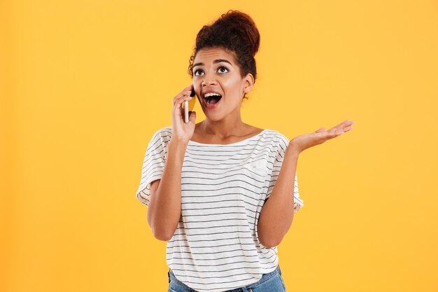 Heureuse jeune femme africaine avec la bouche ouverte, parler au téléphone isolé