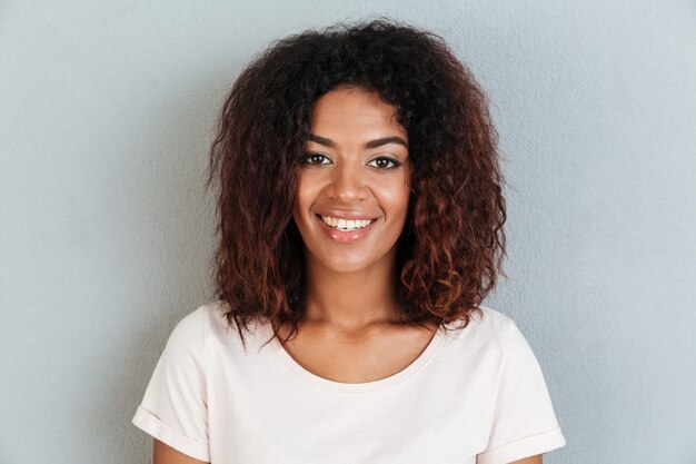 Heureuse jeune femme africaine debout sur un mur gris.