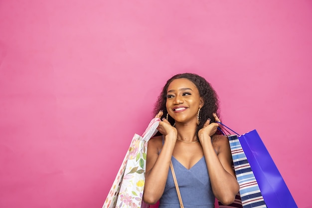 Photo gratuite heureuse jeune femme africaine posant avec des sacs à provisions isolés sur un rose